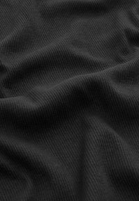 Tissu noir côtelé au toucher doux, affichant des vagues et des plis subtils. La surface présente de fines lignes verticales tout au long.