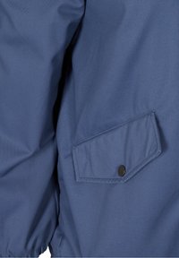 Sininen kangastakkihiha, jossa on läppätasku, joka suljetaan yhdellä mustalla ponnahdusnapeilla, ja joustava hihansuu ranteessa.