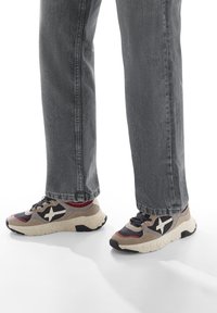 Sneaker con un design grigio, rosso e nero, dotate di una suola spessa e logo a stella bianca, indossati con jeans dritti grigi.