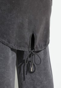 Top de corte holgado en gris carbón con un acabado texturizado, que cuenta con una abertura lateral y un detalle de cordón en el dobladillo. Tejido suave y casual.
