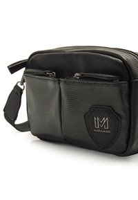Bolso cruzado sintético negro con textura, que cuenta con dos bolsillos frontales con cremallera, una correa para el hombro y un parche de logo de la marca.