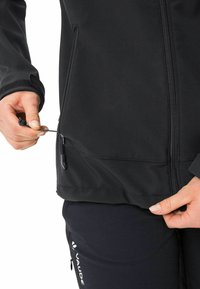 Giacca softshell nera con una tasca con zip in vita, orlo regolabile con cordino e una texture liscia adatta per attività all'aperto.