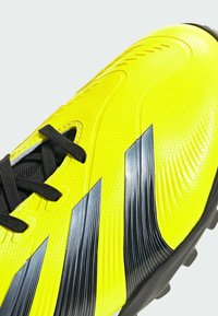 Chaussure de soccer jaune vif avec une surface texturée, des lacets noirs et des accents noirs angulaires. Présente un design épuré et aérodynamique ainsi qu'une semelle extérieure en caoutchouc.