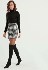 Maglietta nera a maniche lunghe abbinata a una gonna corta a motivo houndstooth bianca e nera, completata da stivali neri con tacco al ginocchio.