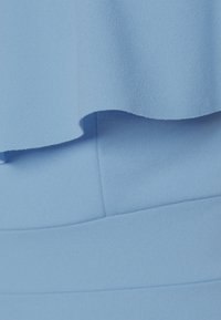 Haut en tissu bleu clair avec un ourlet évasé, présentant une texture lisse et des coutures nettes. Le design est superposé avec une pièce de taille unie contrastante.