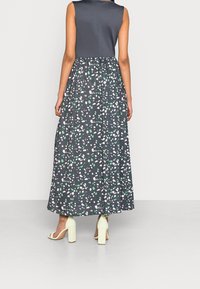 Sukienka bez rękawów z dopasowanym granatowym topem i długą, zwiewną spódnicą z ciemnym wzorem zielonych i białych nieregularnych kształtów.