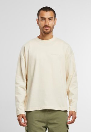 Cream-colored long-sleeve shirt made of soft fabric, featuring a crew neckline and a relaxed fit, paired with olive green cargo pants.