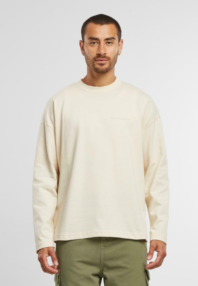 Camisa de manga larga color crema hecha de tela suave, con cuello redondo y un corte relajado, combinada con pantalones cargo de color verde oliva.