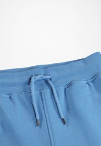 Modre trenirke z ribanim pasom, nastavljivo vrvico in gladko teksturo. Opazni kovinski detajli na koncu vrvice.