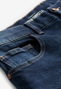 Blugi din denim albastru închis, cu talie medie, design clasic cu cinci buzunare, detalii din hardware de culoare cupru și cusături contrastante.