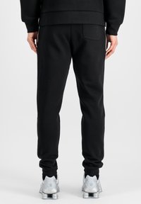 Zwarte sweatpants met een toelopend ontwerp, elastische tailleband en een achterzak, gecombineerd met zilveren sportschoenen tegen een effen achtergrond.