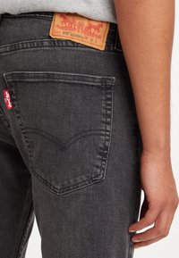 Svarta jeans i denim med klassisk design med fem fickor, detaljer i sömmen på bakfickan och en ljusbrun läderlapp med röd märkning.