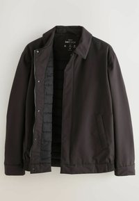 Schwarze wasserdichte Jacke mit einem Reißverschluss und Druckknöpfen. Verfügt über ein gesteppte Innenfutter und Seitentaschen, mit einem elastischen Saum.