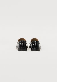 Mocassins en cuir noir au design minimaliste, à bout rond, petit talon et intérieur beige. Présentent un accent de boucle en métal de chaque côté.