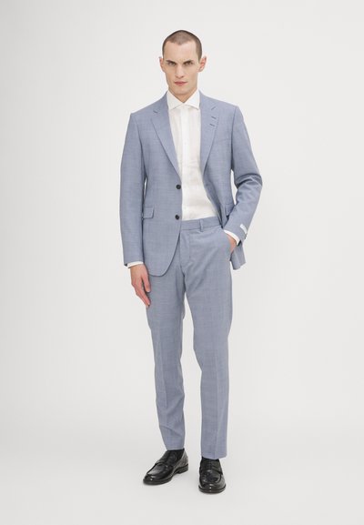 Completo azzurro chiaro in tessuto texturizzato, giacca monopetto e pantaloni con frontale piatto. Abbinato a una camicia bianca e scarpe nere.