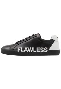 Sneaker nera basse con tallone bianco e grande testo bianco "FLAWLESS" di lato, caratterizzata da lacci neri e suola nera.