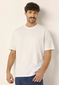 Hvid bomulds T-shirt med korte ærmer, rund hals og løs pasform. Stoffet er glat, og designet er minimalistisk uden mønstre.
