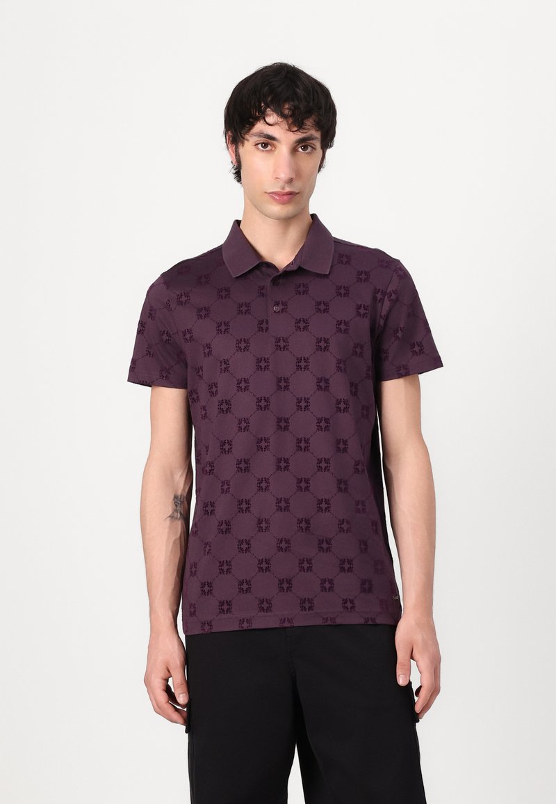 Lila polo majica z diskretno patternirano zasnovo z izrazitimi oblikami. Kratke rokave, klasičen ovratnik, izdelana iz mehkega blaga.