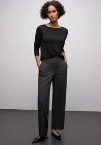 Schwarzer Strickpullover mit rundem Ausschnitt, kombiniert mit hoch taillierten dunkelgrauen Hosen mit subtiler Textur und lockerem Schnitt. Schwarze Loafers.