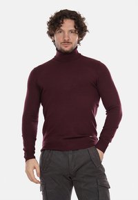 Maglione a collo alto color borgogna realizzato in tessuto a maglia liscia; design aderente con maniche lunghe e polsini a costine, con un piccolo logo dettagliato sull'orlo.