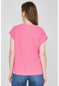 T-shirt in cotone rosa con maniche corte, scollatura rotonda e vestibilità comoda. Il tessuto ha una texture morbida e una finitura liscia.