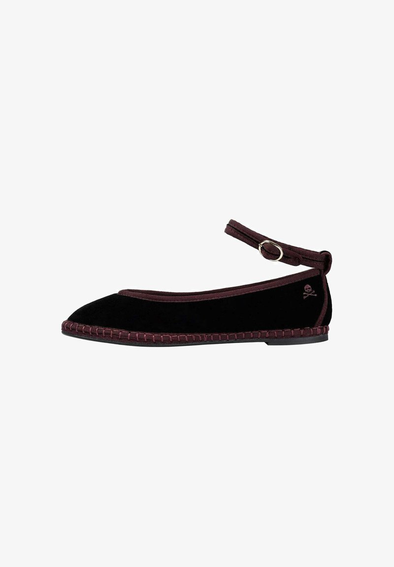 Zapato plano de terciopelo negro con una correa de tobillo burdeos, con un borde trenzado a lo largo de la suela y un pequeño detalle de logo en el talón.
