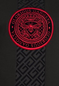 Patch ricamato rosso e nero con emblema di corona e ape, circondato dal testo "GLORIOUS GANGSTA" su un tessuto scuro con motivo geometrico.
