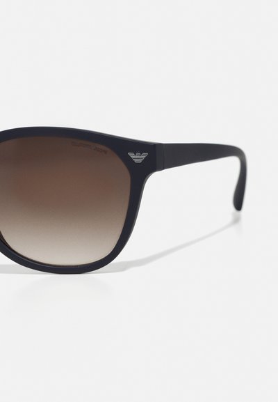 Ochelari de soare negri cu lentile degradate maro și un design elegant. Prezintă un logo argintiu pe ramă. Material neted și formă modernă.