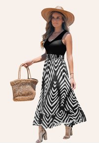 Robe maxi à rayures en chevron noir et blanc avec un haut ajusté, une jupe évasée et un bord volé, associée à un sac en paille tressé et des sandales à talons.