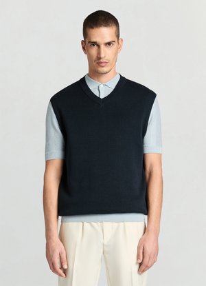 Gilet en tricot bleu marine avec un col en V porté sur une chemise à manches courtes bleu clair. Texture lisse et coupe décontractée. Pantalon slim visible.