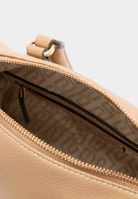 Hnědá kožená taška s zipovým uzávěrem, má podšívku s vzorovanou látkou a zlatý zip. Hladký povrch, minimalistický design.