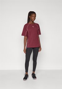Burgunderfarget treningst-skjorte med hvite sømmer, kortermer og rund hals, paired med svarte leggings og svarte treningstøvler.
