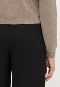 Light beige knit sweater with ribbed hem, worn over black pants. Features a close-fitting design and smooth texture.