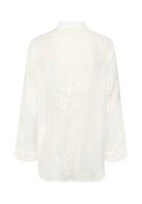 White embroidered blouse with a soft texture, featuring a collar, long sleeves, and floral patterns on the fabric. Buttoned cuffs visible.