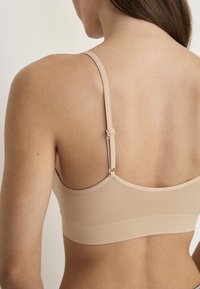 Beige mesh-bralette med justerbare stropper, blød tekstur og sømløst design. Har en minimalistisk stil uden synligt hardware.