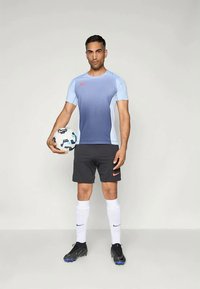 Nike sportska majica u gradijent plavoj boji, crne kratke hlače, bijele čarape, crne kopačke. Igrač drži šaru loptu za nogomet s Nike logotipom.