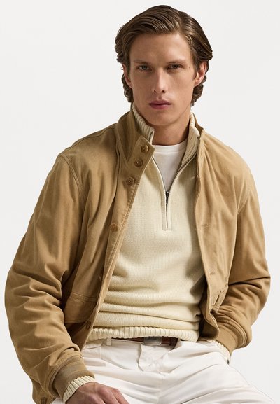 Veste beige au toucher doux et à fermeture à boutons, associée à un pull crème en côtes et à un pantalon clair. Design simple, teintes neutres.