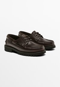 Bruine leren bootschoenen met een gladde afwerking, ronde neus, vetersluiting en een gestructureerde zwarte rubberen zool. Verstevigd met metalen oogjes.