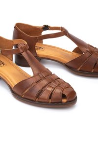 Sandalias de cuero marrón con punta abierta, diseño trenzado y correa en el tobillo. Plantilla acolchada y tacón bajo y robusto.