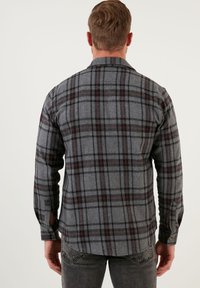 Camicia a quadri grigia con linee rosse e nere, realizzata in tessuto strutturato. Presenta maniche lunghe, colletto a bottoni e polsini rinforzati.