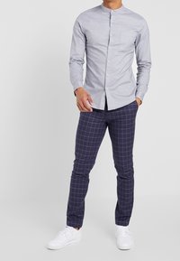 Ljusgrå långärmad skjorta med knappar, ståkrage och bröstficka. Matchat med marinblå rutiga byxor och vita sneakers.