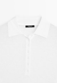 Polo en maille blanche avec cinq boutons et un col, avec une étiquette noire "Massimo Dutti" au niveau de l'encolure.