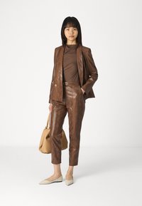 Bruin met slangenprint pak met een getailleerde blazer en broek. Bruine top eronder, beige ballerina's en een beige handtas. Gladde textuur.