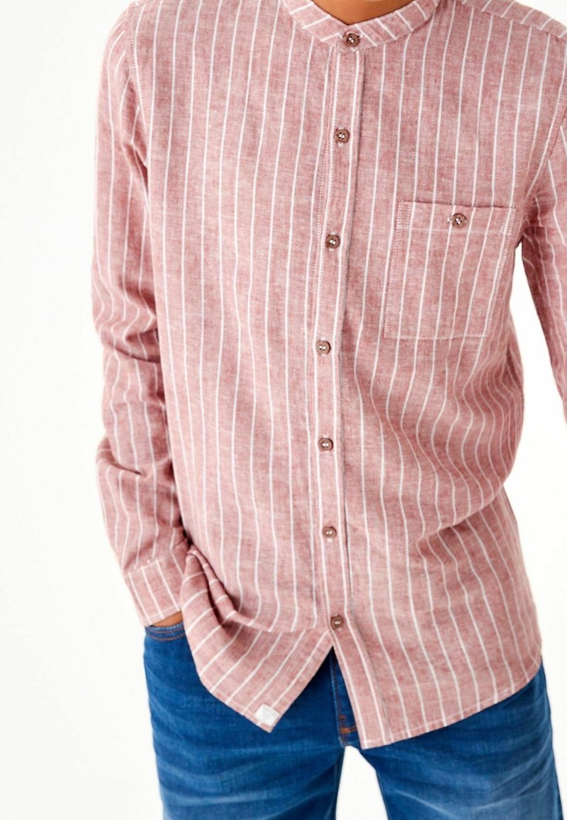 Chemise boutonnée en tissu rouge délavé avec des rayures verticales blanches, col arrondi, une poche poitrine et des boutons marron.