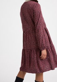 Robe à motifs rouges avec manches longues, ourlet à volants et taille élastique. Présente un motif floral en crème et bleu foncé. Texture de tissu douce.