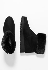 Botas de tobillo de ante negro con un lujoso puño de pelo sintético, superficie texturizada y suela de goma estriada para mayor tracción.