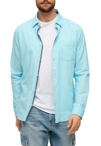 Helles blaues Langarmhemd mit Button-Down-Kragen, das über eine Brusttasche und einen kontrastierenden dunklen Besatz entlang der Knopfleiste verfügt.