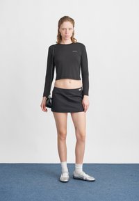 Czarny krótki top z długim rękawem, czarna mini spódnica, srebrne płaskie buty, białe skarpetki z falbaną oraz mała czarna torba na ramię. Prosty design, bez wzorów.