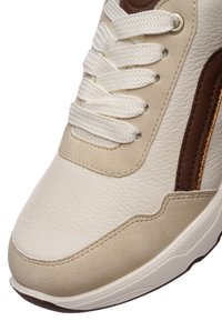 Béžová a krémová teniska s textúrovaným koženým zvrškom, plochými bielymi šnúrkami a hnedým bočným prvkom s kovovým zlatým pruhom.