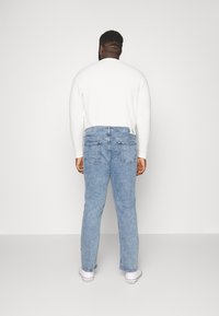 Jeans de mezclilla azul claro con corte recto, cinco bolsillos y una ligera textura desteñida, combinados con una camiseta blanca de manga larga lisa.